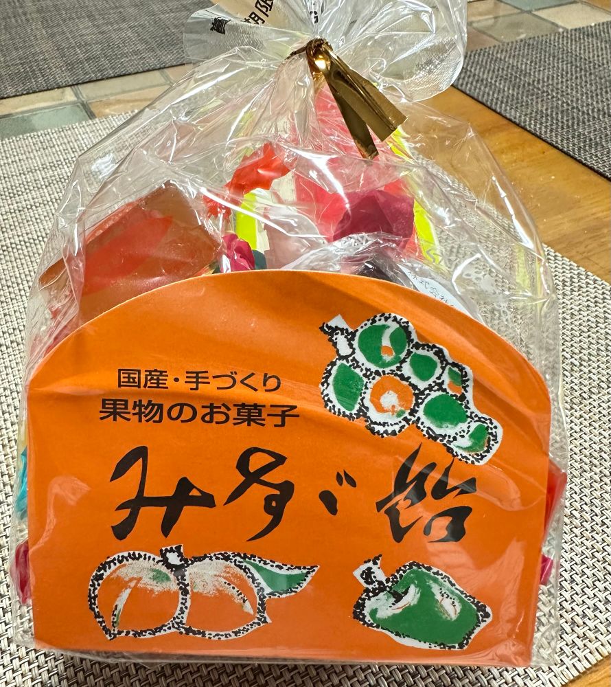 個包装されたカラフルなゼリーが入った透明な袋。果物のイラストが描かれたオレンジ色のラベルには「みすゞ飴」と大きく書かれ、その上には「国産・手づくり」「果物のお菓子」の文字が見える。