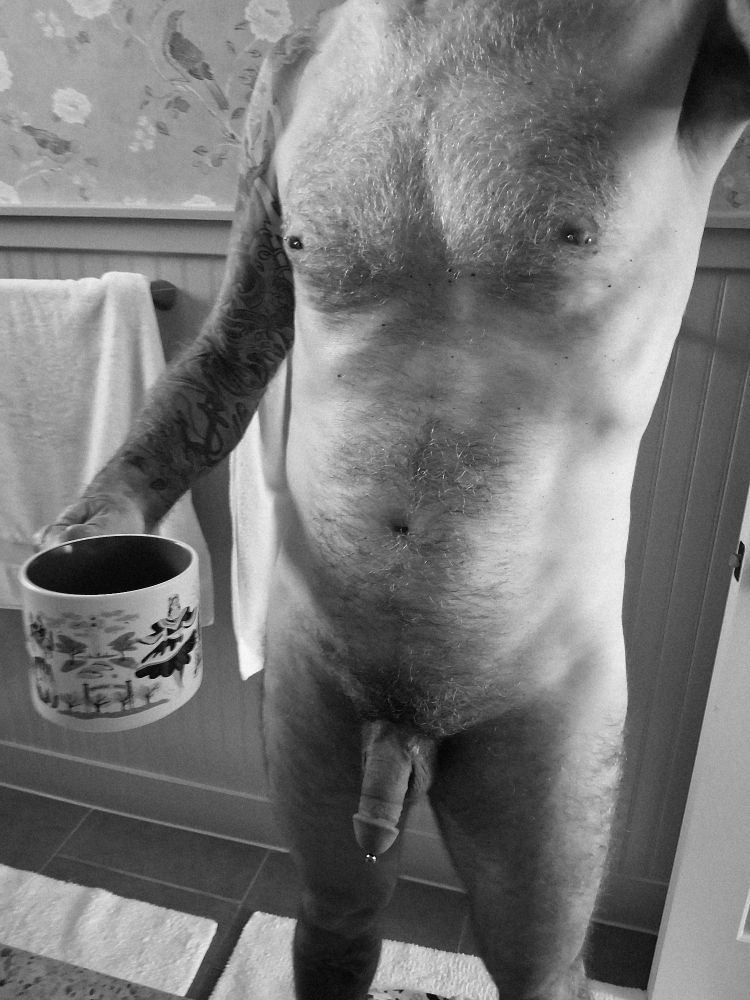Nude pierced and tattooed guy with coffee cup