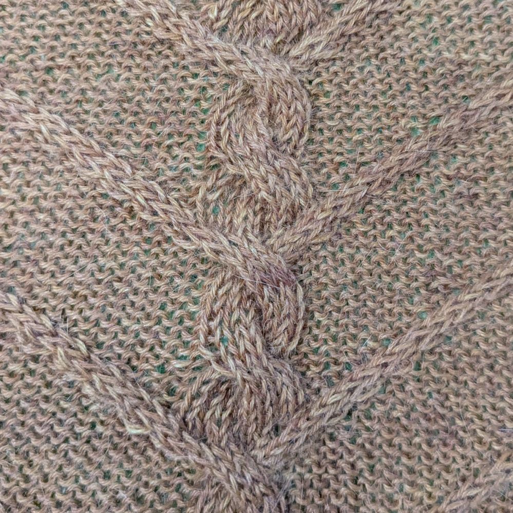 A close up of a hand-knit piece. It features a thick center cable with thinner cables branching off at regular intervals against a reverse stockinette background