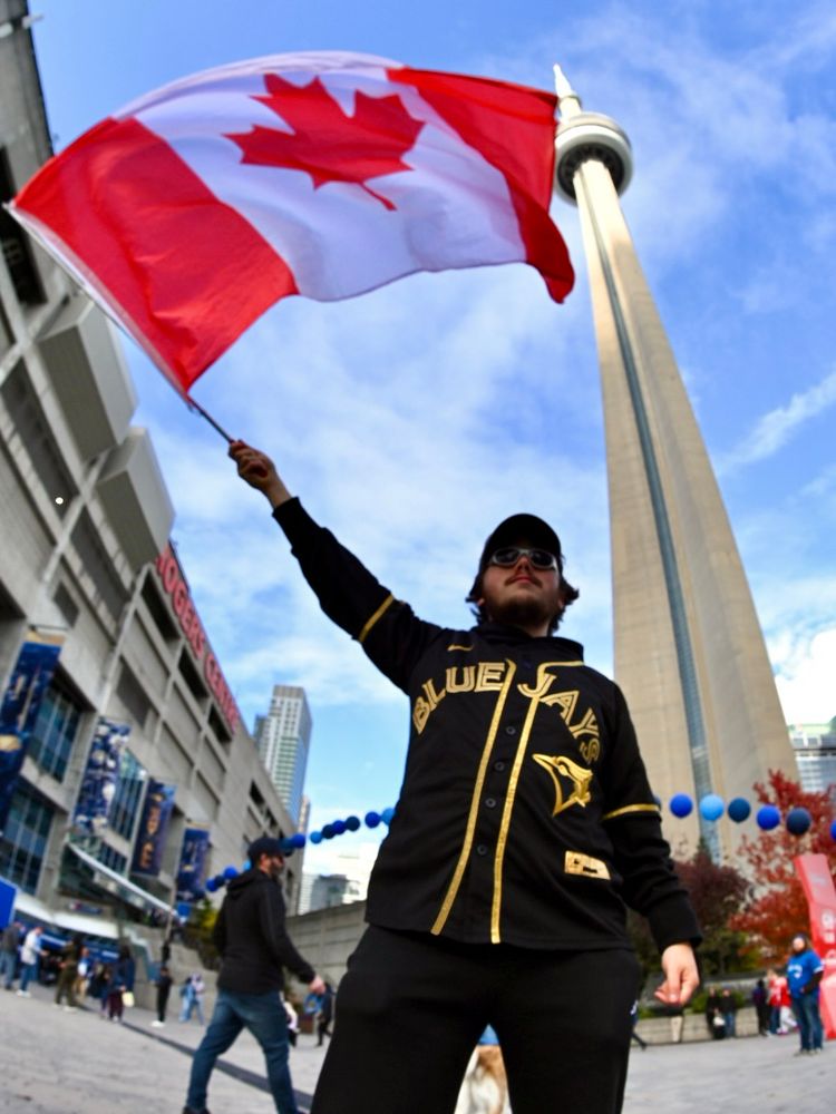 A Toronto Blue Jays fan waves the Canadian flag above his head. Behind him is the CN Tower. 