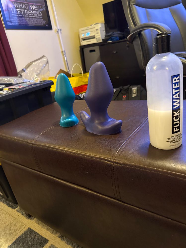 A snuckle 26 and 30 sit on an ottoman with a tall bottle of lube.