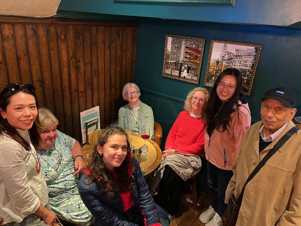 Group of seven people smiling and sitting around a table in a pub, with pictures on the wall behind them.