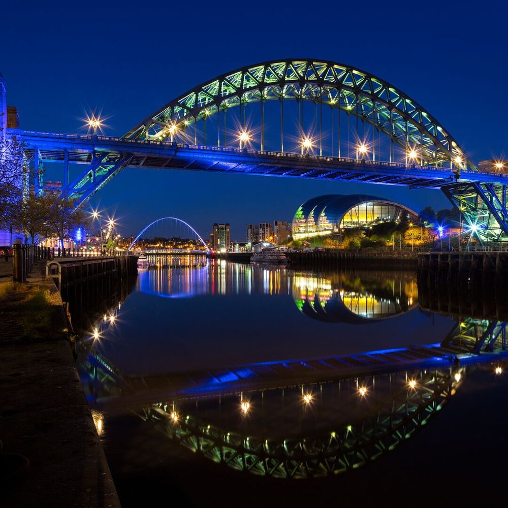 picture of the Tyne Bridge and Millennium Bridge over the river in the night with shiny lights