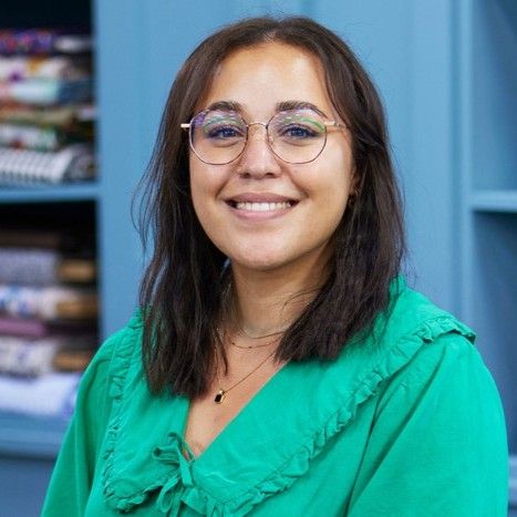 Person in a green top and glasses smiling in front of a bookshelf.