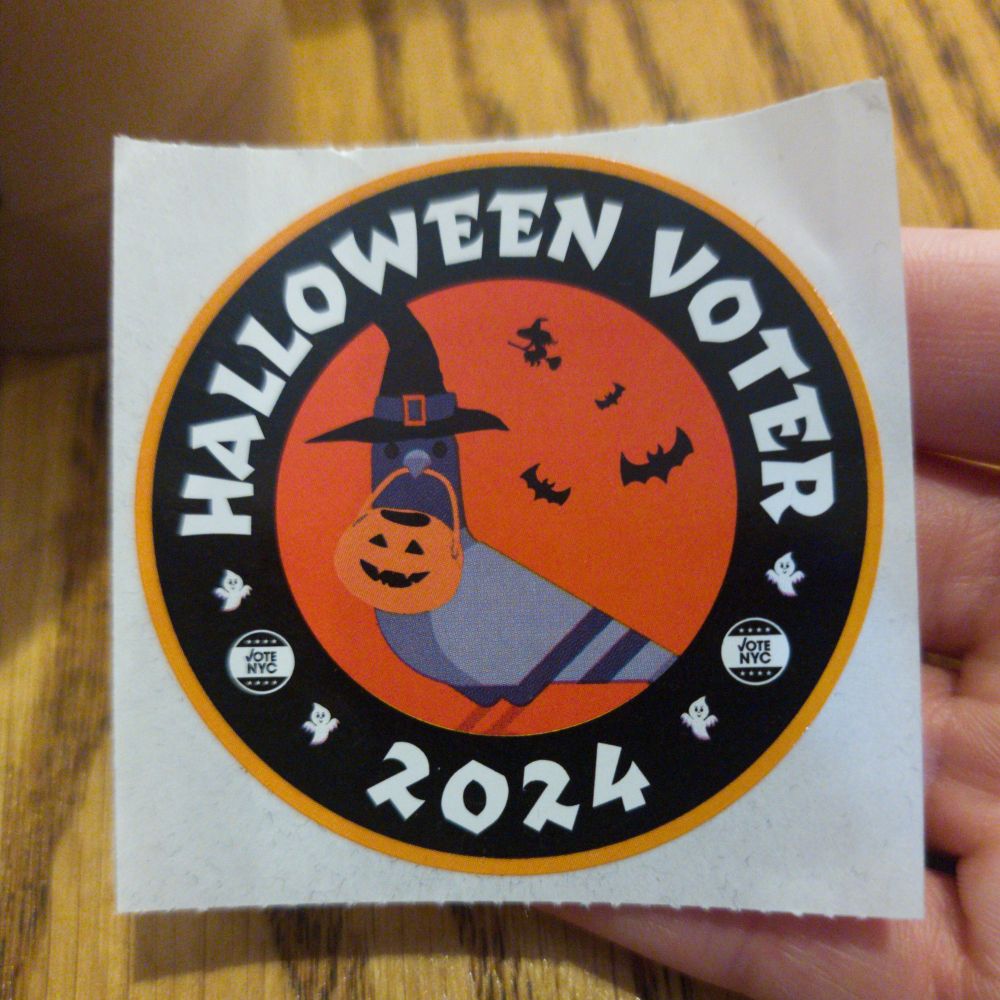An I Voted NYC sticker, which says 'Halloween voter 2024' around the outside and has a pidgeon dressed as a witch and carrying a pumpin shaped candy bucket in the center
