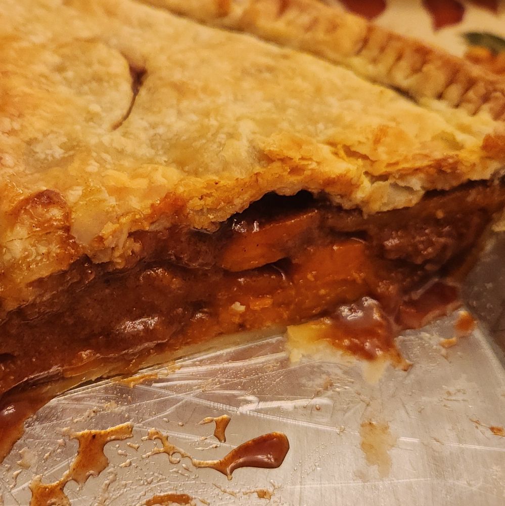 A double crust pie sliced open in an aluminum pie tin. From the open side it can be seen that this is not a mashed sweet potato pie but that the sweet potatoes are layered in slices, with syrup