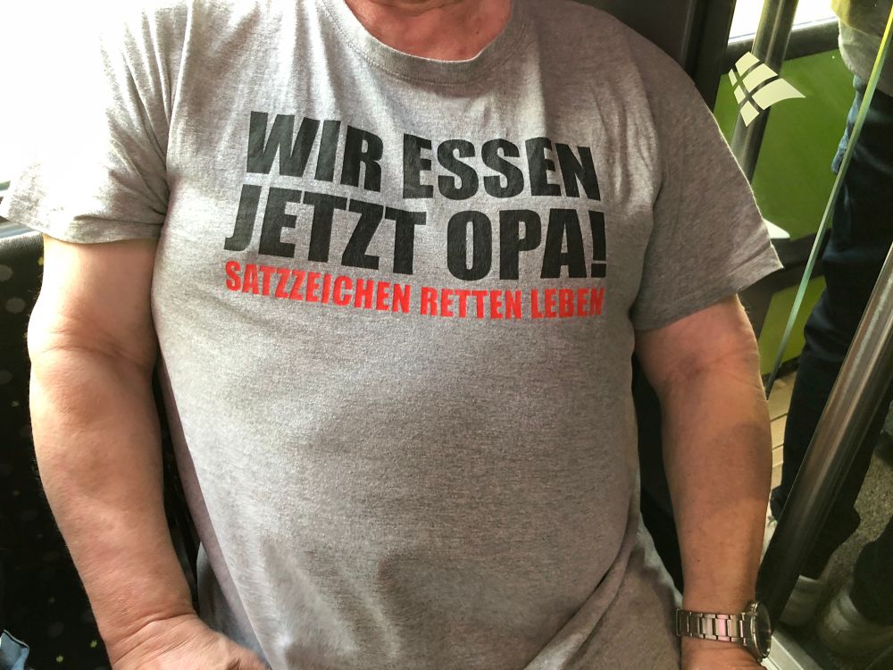 T-Shirt über breiter Männerbrust. Aufdruck: „Wir essen jetzt Opa!“. Kleiner darunter: „Satzzeichen retten Leben“.