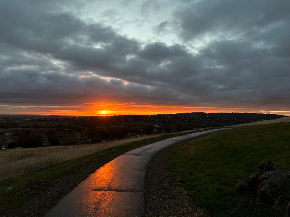 Sunset over a paved bike trail, still wet with today's rain. You feel serene.