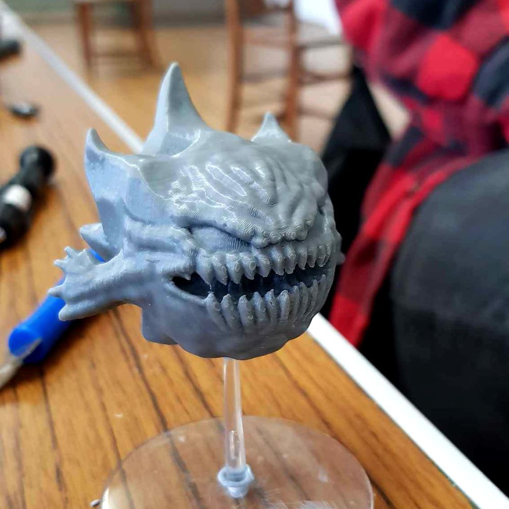 The bomb sculpture has been 3D printed in grey filament. Much of the detail is preserved, but print lines are more visible around the mouth and eyes. It is held aloft using a "flying base", a plastic transparent disk with thin column that protrudes from the center. The model rests on the column, giving the illusion of levitation.