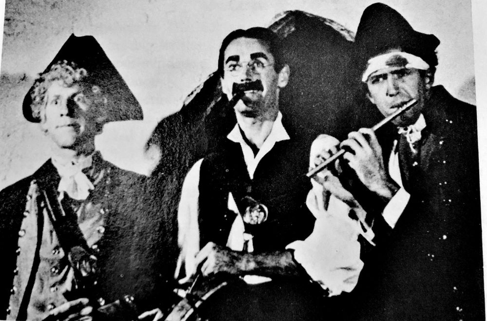 The three men are dressed as the Marx Brothers, Swope as Harpo, Fonda as Groucho, Stewart as Chico. They’re dressed in American Revolution garb, recreating the painting Spirit of ‘76 by Archibald Willard. Photo by John Swope, printed in Howard Teichmann’s biography of Henry Fonda.