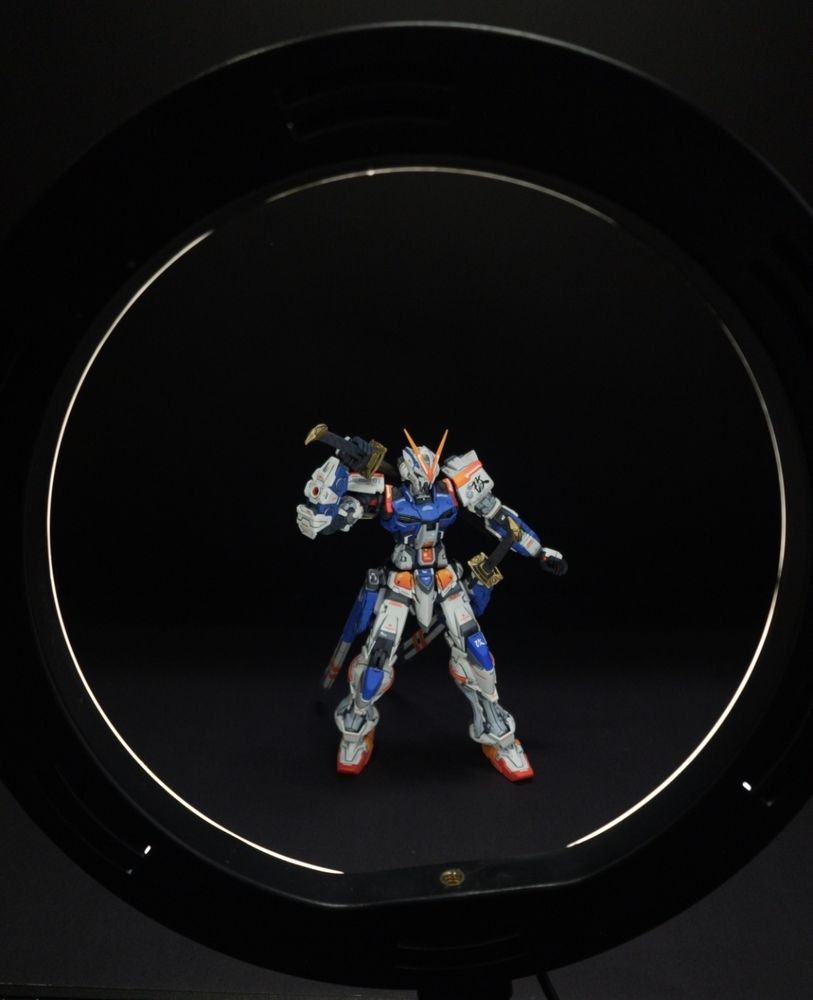 A repainted Astray Red Frame gundam model on a black background framed by a ring light