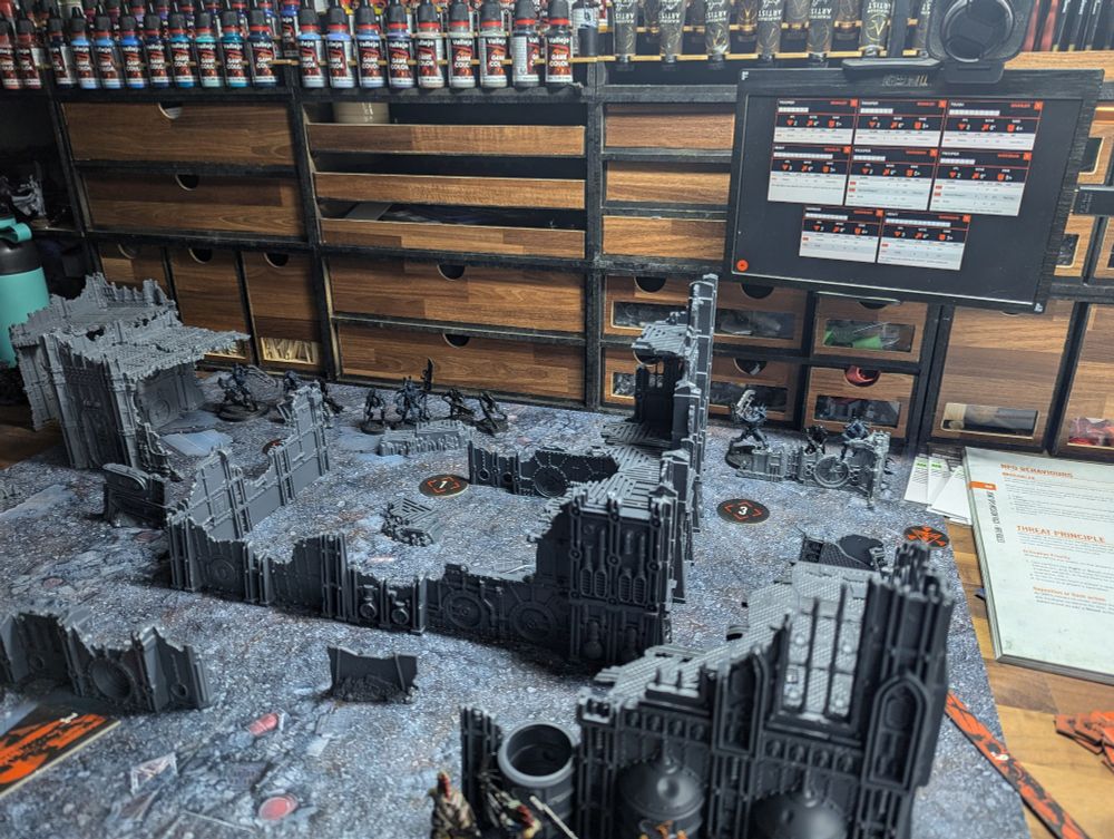 A set up game of Kill Team with a small screen displaying a website for tracking the health of non-player operatives