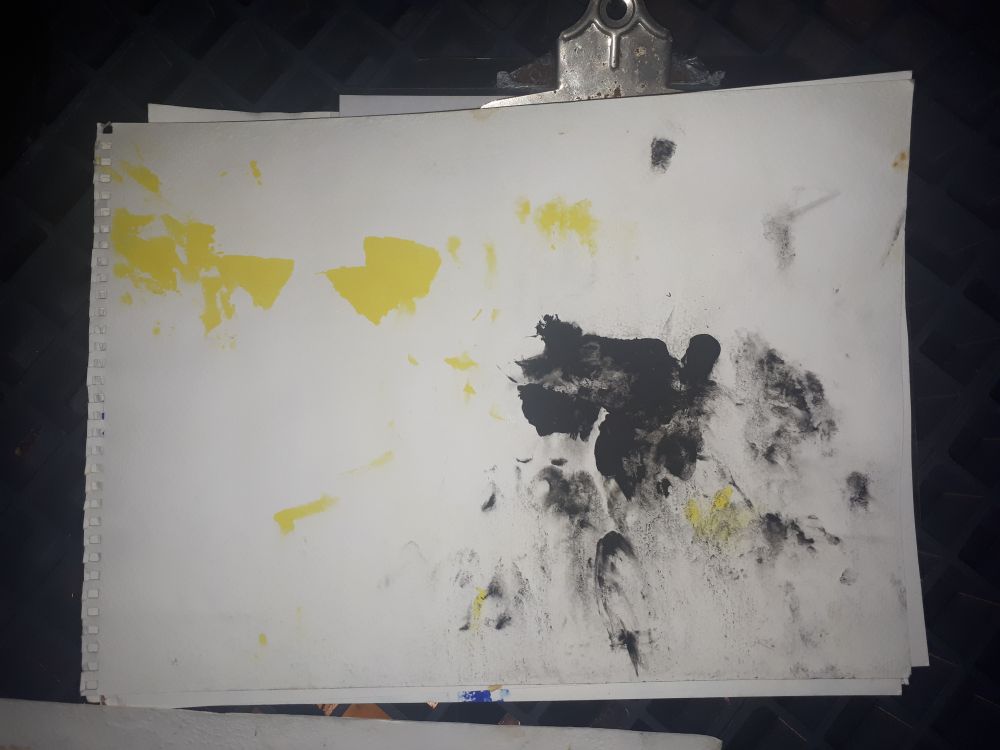 A piece of paper with splattered paint over it attached to a clipboard, it is black and yellow.