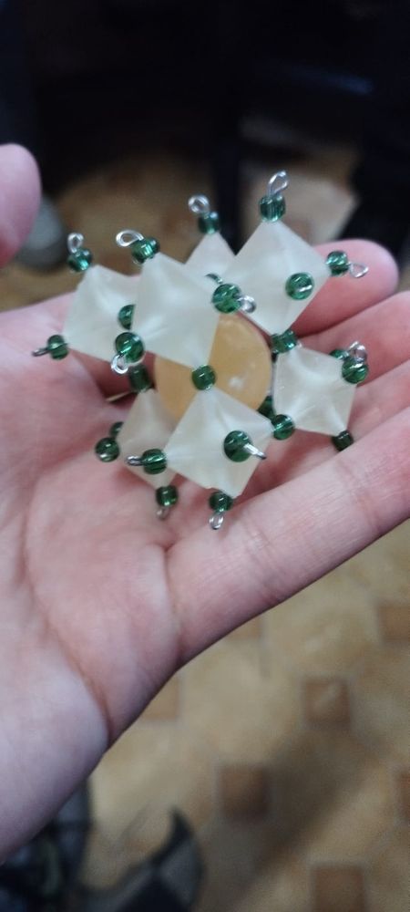 One hand holding Perovskite model made out of 8 resin octahedra connected with green beeds and a yellow sphere in the hole left by the octaedron
