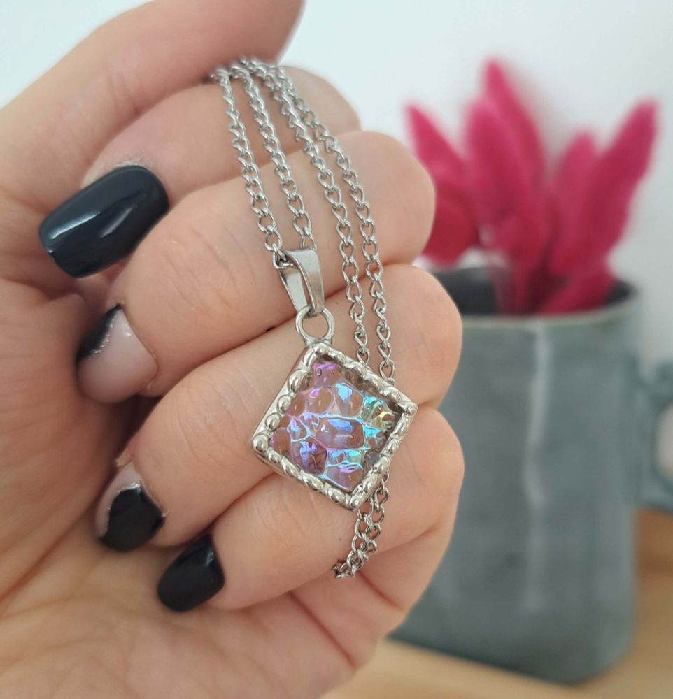 Collier composé d'un pendentif carré en verre irisé encadré d'étain pur selon la méthode tiffany. Une chaine en acier inoxydable l'accompagne.