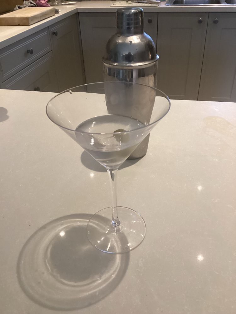 Martini glass with olive and cocktail shaker in the background
