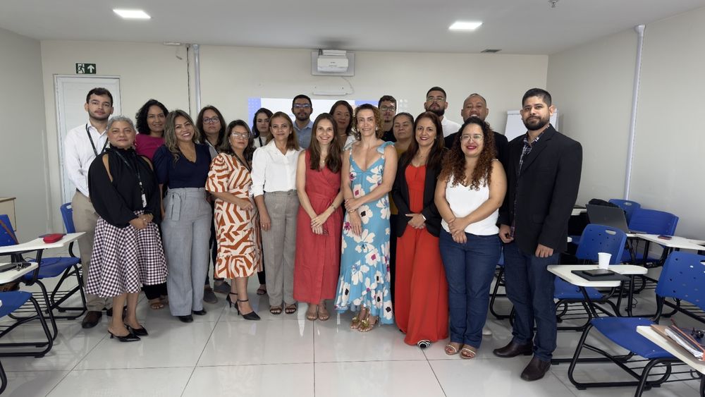 Imagem mostra grupo de pessoas, em pé, no centro de uma sala de aula.