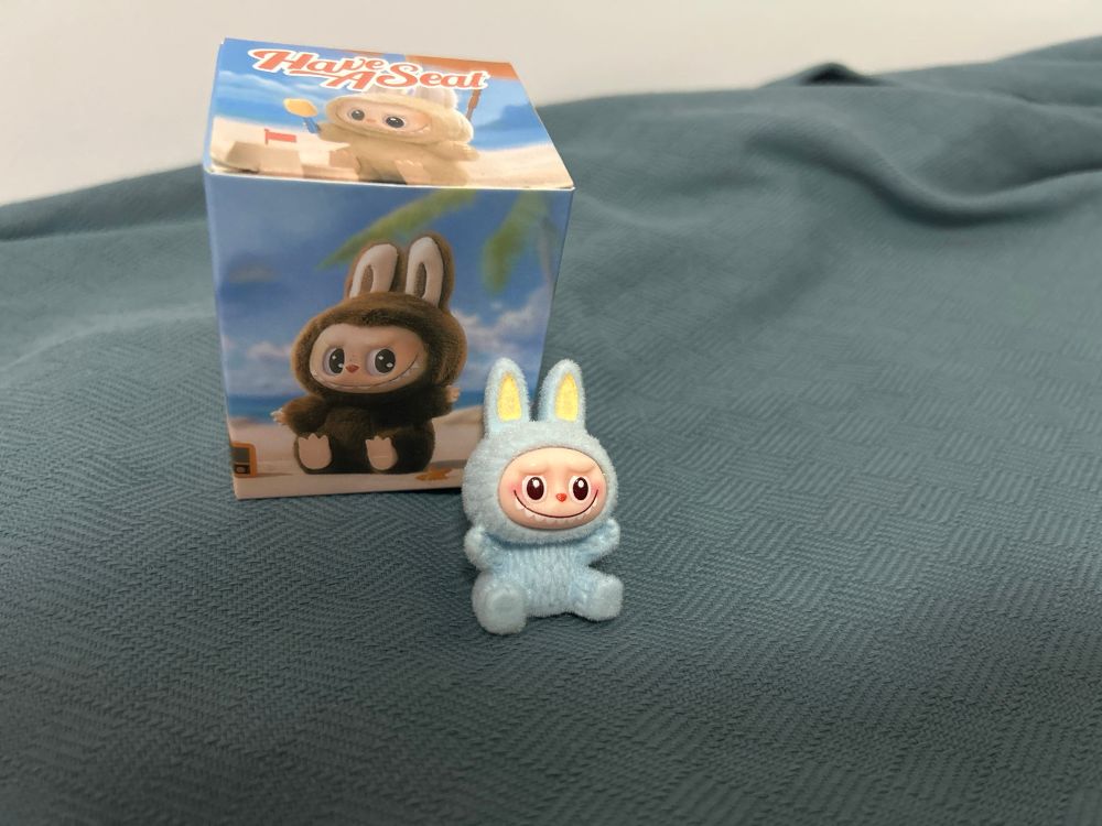A small Labubu doll from the Have A Seat collection. It's blue with yellow in the ears. 