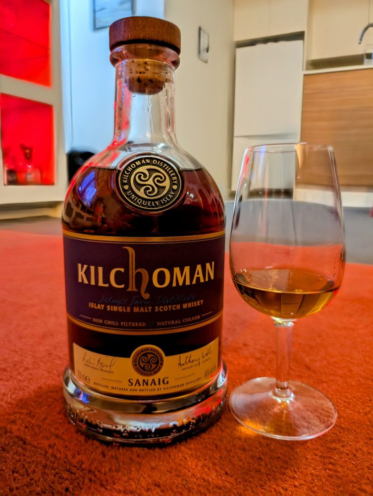 A bottle of Kilchoman Sanaig peated whisky and a stemmed whisky glass of the same.