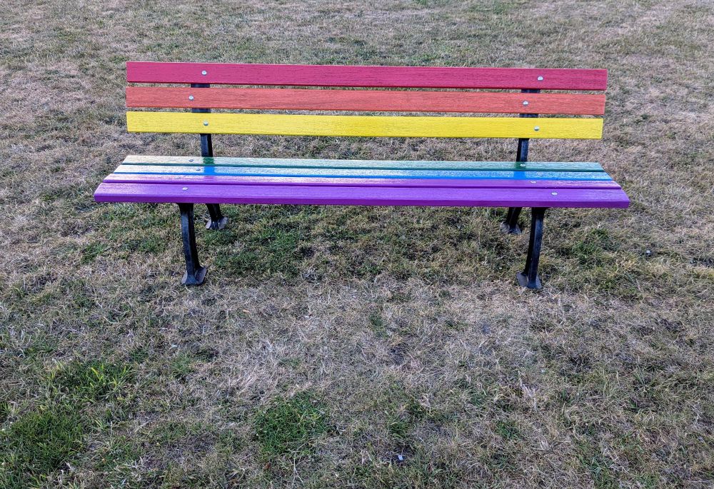 Sitzbank in Regenbogenfarben auf einer Grasfläche 