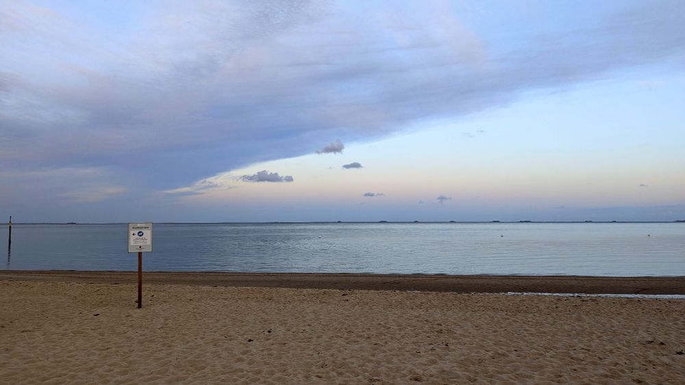 Leerer Strandabschnitt  (Hundestrand ohne Hunde und Menschen) mit Schild (Hinweis auf Hundestrand). Ruhiges Meer (Nordsee) und Wolken am Himmel.