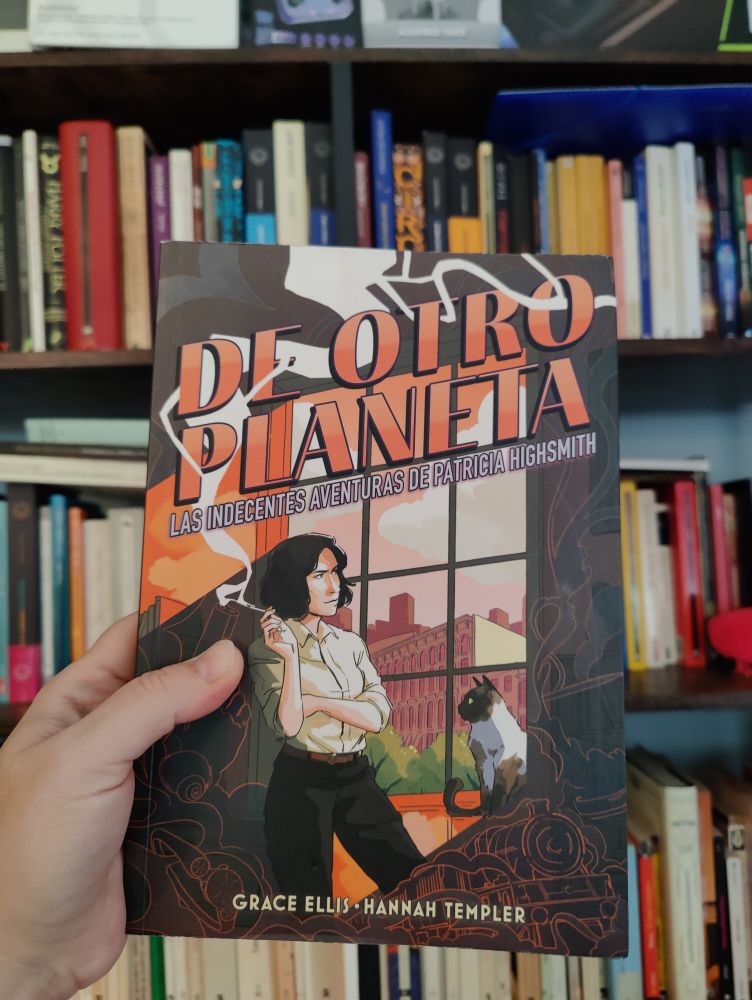 Se ve mi mano sosteniendo el cómic. Detrás puede verse una estantería con libros. En la cubierta del cómic aparece Patricia Highsmith fumando junto a una ventana mientras su gato la mira.