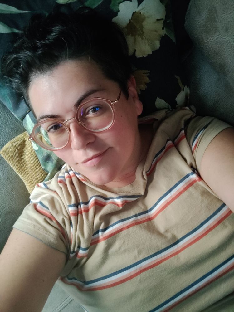 Selfie de cara y torso, tumbada boca arriba en el sofá. Llevo una camiseta color crema con rayas de colores