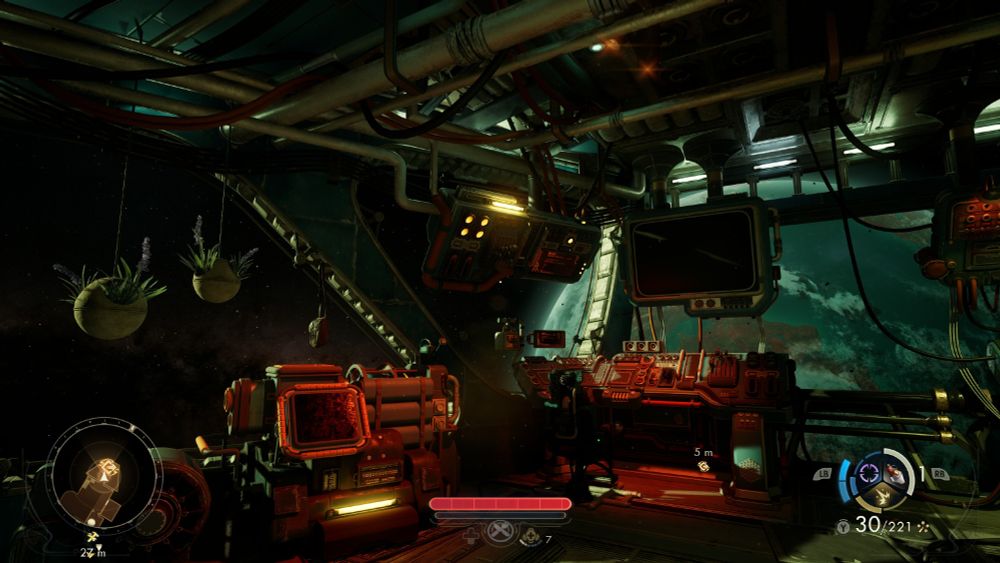 El interior de una nave rudimentaria con paneles, monitores, cables gruesos y tuberías colgando del techo. De una de las tuberías del techo cuelgan dos macetas.