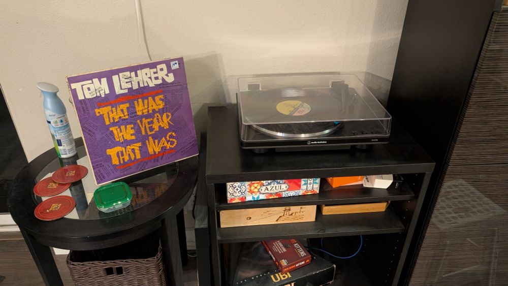 A record player playing a record. A record stand nearby holds the cover; the album is Tom Lehrer's "That was the Year that was"