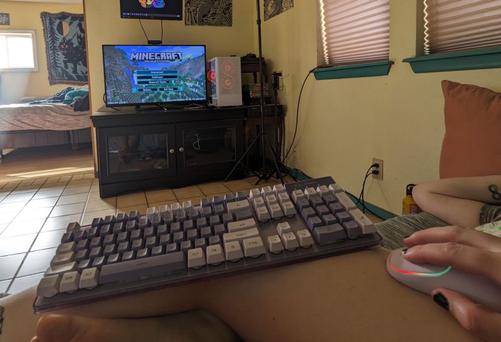 A picture of a mouse and a keyboard sat on top of my leg while I lay sideways, facing the computer while Minecraft is on the screen 