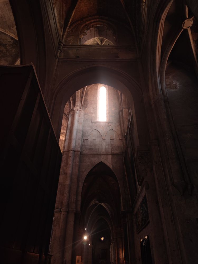 Vue sur le collatéral coupé par le transept et baigné de la lumière d'un vitrail 