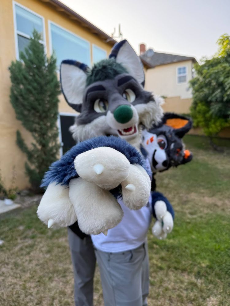 Vataqun pointing to the camera with Shu peeking out from behind. They are standing in a backyard.