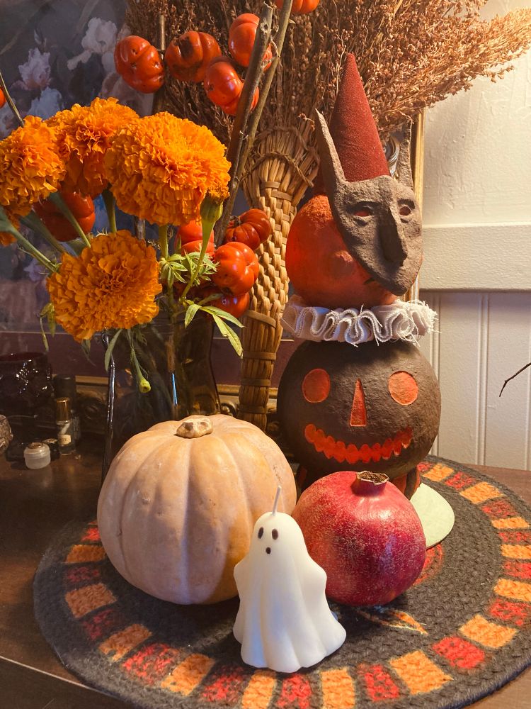 halloween decor arranged on a banquet: a small ghost candle, pomegranate, pumpkin, marigolds, and a papier mache sculpture of two stacked pumpkins 