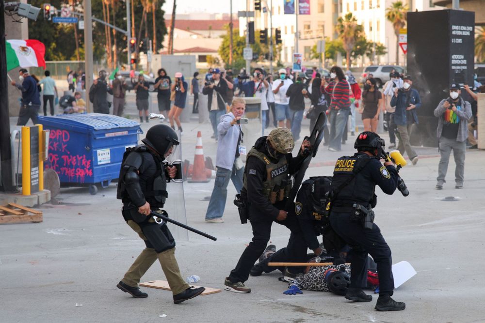 Masked, armored unidentified men carrying wrapons attack a person carrying a protest sign. Four on one