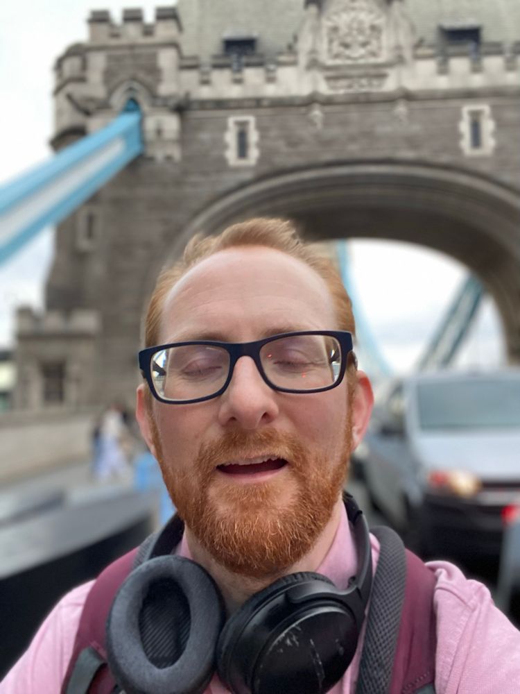 An idiot not smiling and closing his eyes whilst taking a selfie on tower bridge in london.
