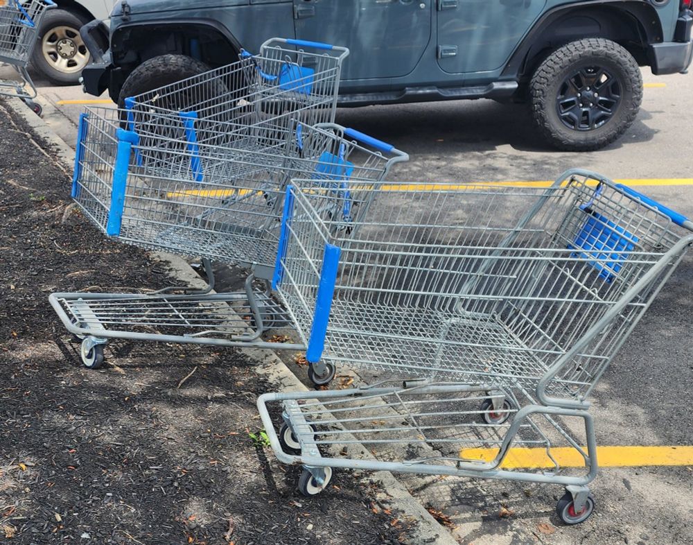 A few shopping carts parked on the curb in a parking lot instead of being returned where they belong to because people are extremely lazy and inconsiderate of others and other employees who may have to come out and pick up those cards