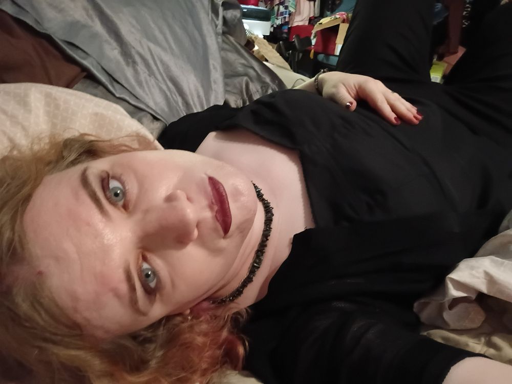 Chi, in the closest thing to a thirst trap photo she'll share with you. She's reclining on a bed in her black sweetheart top and black jeans, with black accessories, smoky makeup, and a dark red lip. Her eyes are so goddamn big and blue and you could fall into them.