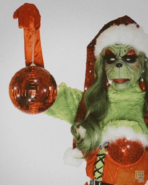 Cunty grinch holding a red disco ball 