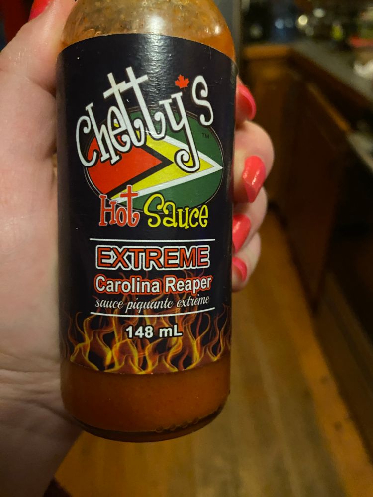 A bottle of hot sauce being held in a hand, it reads: 
Chetty’s Hot Sauce. 
EXTREME 
Carolina Reaper
sauce piquante extrème
148mL

Back reads
Made in Canada