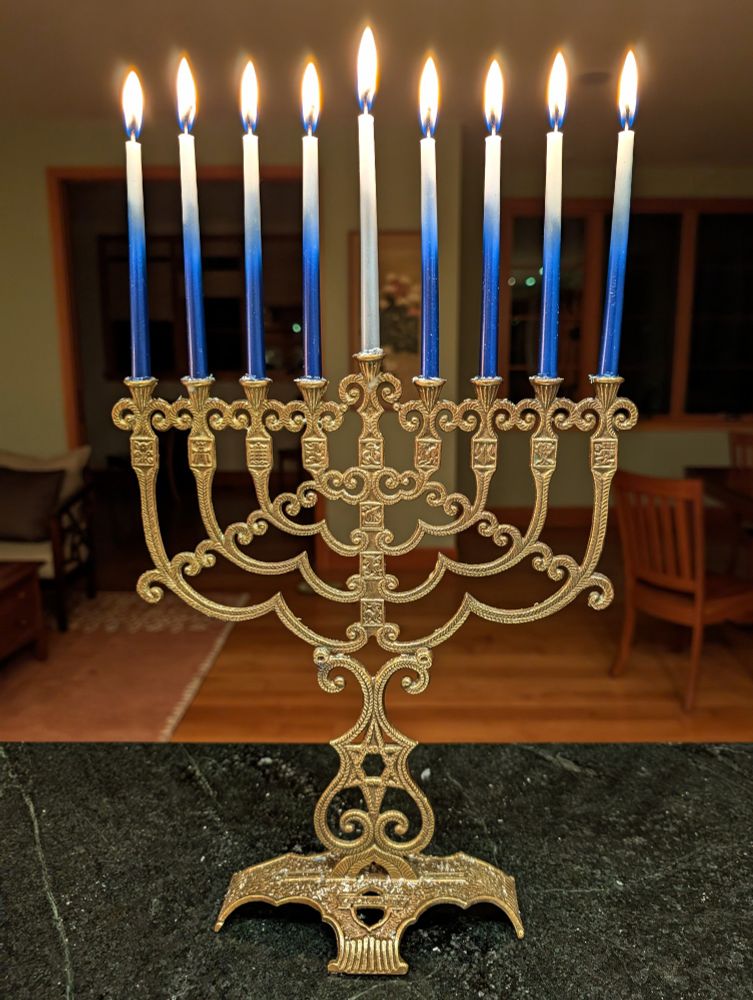 Brass chanukiah with eight lit blue/white candles and a silver/white shamash candle in the middle 