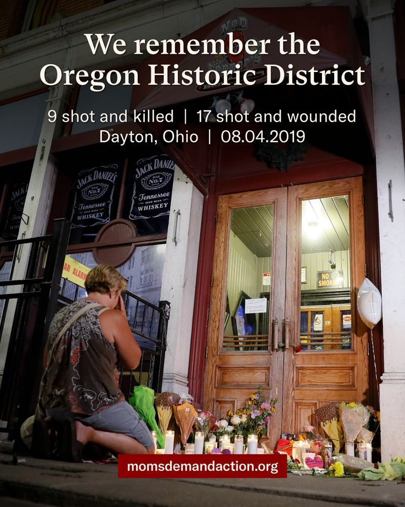 A woman kneeling in front of a makeshift memorial with flowers and candles in a doorway in downtown Dayton, Ohio. Text reads "We remember Dayton, Ohio, 9 shot and killed, 17 shot and wounded, August 4, 2019. momsdemandaction.org"