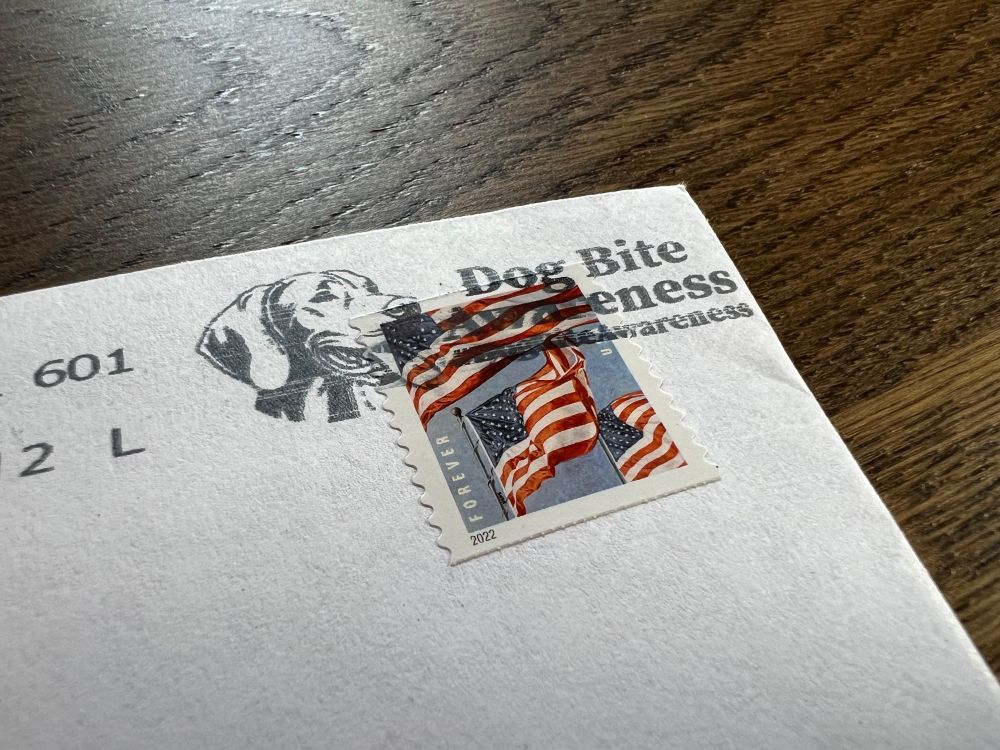 The corner of an envelope with a US flag stamp. The cancellation features a dog face and the words “Dog Bite Awareness #DogBiteAwareness”