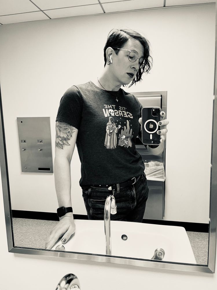 That same mirror selfie I keep posting. Long hair cascades to my right side with the short left side in a pixie length. I’m looking down toward the phone in a kind of demure way, my hand resting against the bathroom sink. 

My tits look bangin’ underneath a graphic tee.