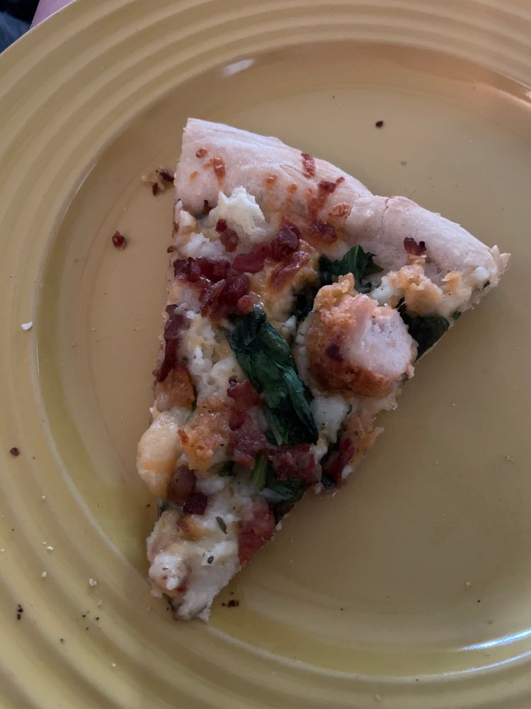 A slice of pizza with bacon, chicken, and mashed potatoes. 