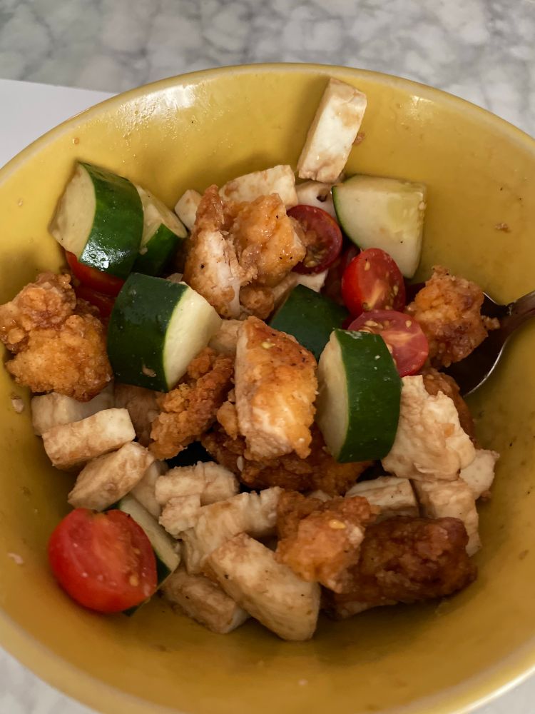 Fried chicken bites, mozzarella, cucumbers, and tomatoes tossed in balsamic in a yellow bowl. 