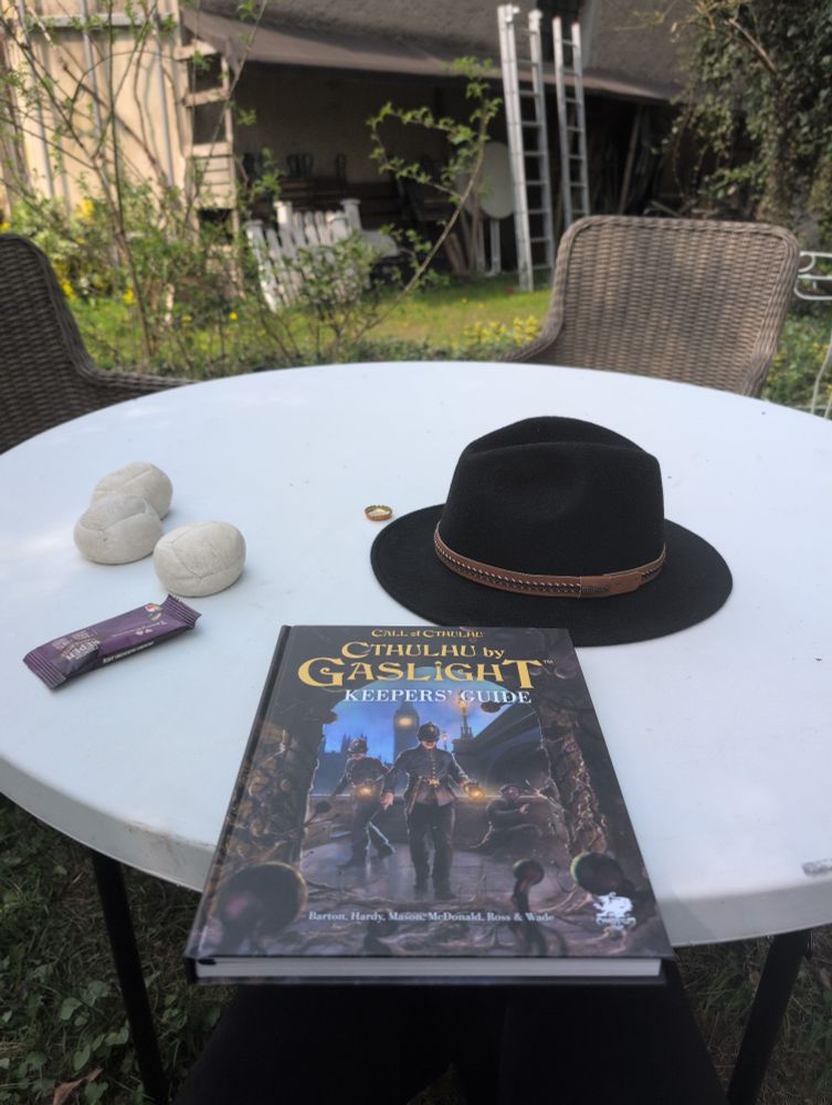 A table with a hat and the call of cthulhu gaslight aera keepers guide on the table