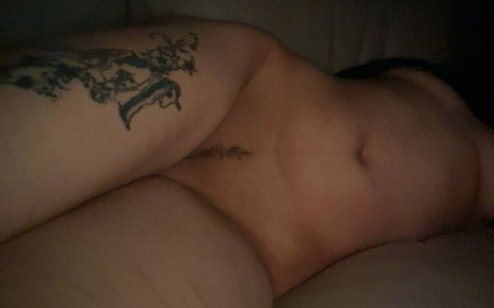 Photo of Finn laying on the couch and on their side. Their thighs just slightly cover their cunt. His shirt is rolled up so his boobs are showing. On Finn’s left thigh there is a tattoo of a unicorn.