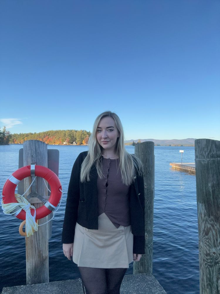 Iona is stood on the jetty of a lake with a life ring beside her
