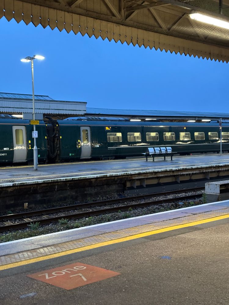 Image at a train station. There is a train on a platform. There is lots of rain. 