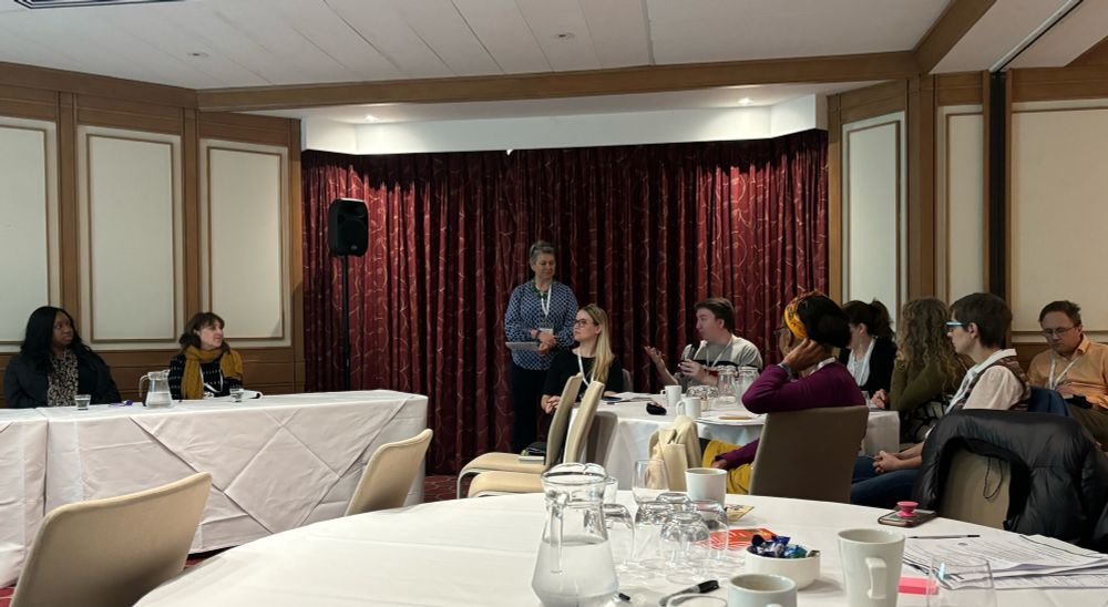 A group of people at a conference. One person hold a microphone as they ask the panel a question.  